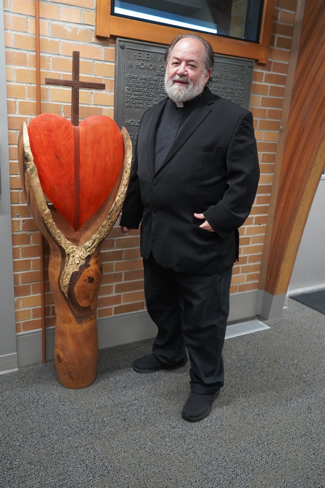 Father David Means, pastor of Most Pure Heart of Mary Parish in Chamois and Assumption Parish in Morrison, stands beside the sculpture he created for the Catholic Charities Center in Jefferson City. He made the sculpture by woodturning a large maple log with two branches in his woodturning shop near the Chamois rectory.